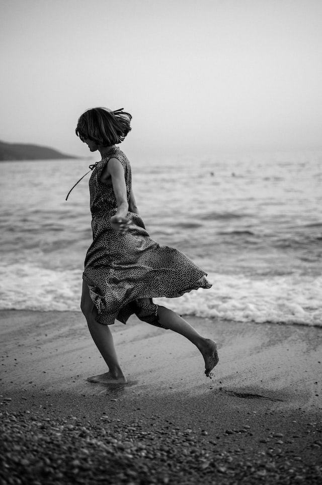 Black and white image of woman in loose dress running on beach